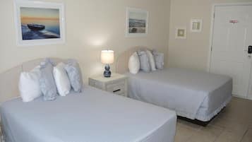 A hotel room with two beds, a nightstand with a lamp, and a door with a 'No Smoking' sign.