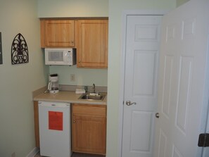 A compact kitchen with wooden cabinets, a microwave, a coffee maker, and a refrigerator.