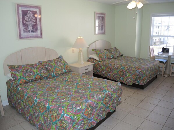 A room with two beds, each with colorful patterned bedding, a bedside table with a lamp, and framed artwork on the walls.
