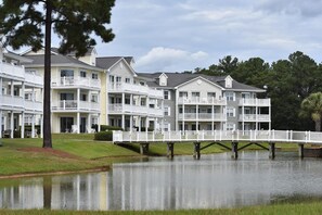 A multi-story hotel with balconies, a dock over water, and a grassy area.