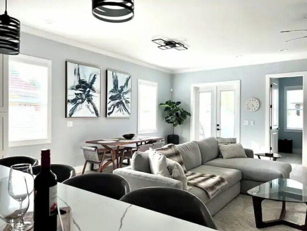 A modern living room with a sofa, a glass coffee table, and a dining area with a table and chairs.
