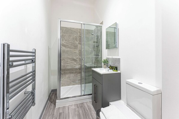 A modern bathroom with a glass shower enclosure, a vanity with a mirror, and a toilet. - Cosy & Convenient 1 Bedroom Apartment in Dudley (Brierley Hill)