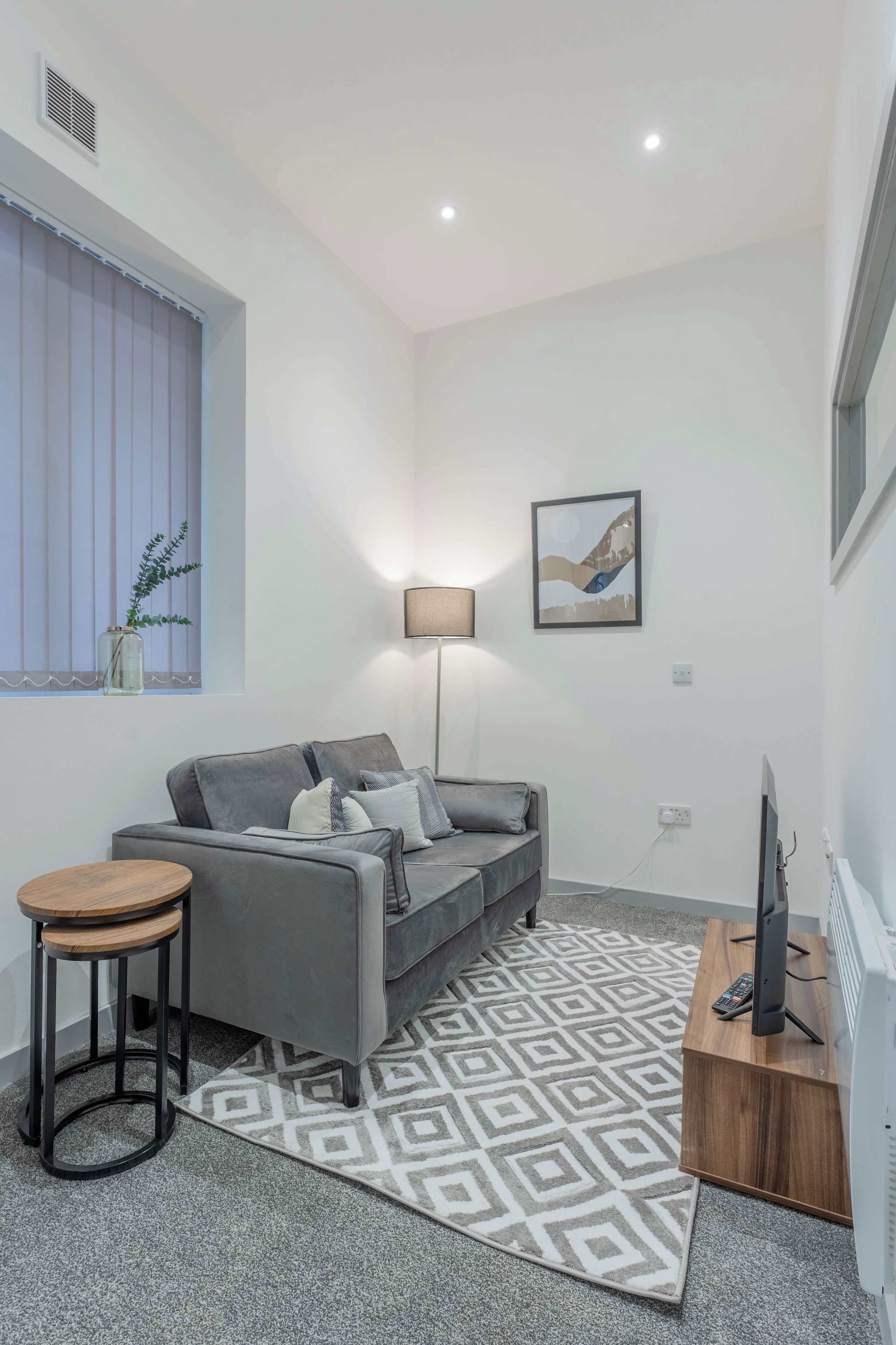 A modern living room with a grey sofa, a small round table, a floor lamp, and a television on a wooden stand.