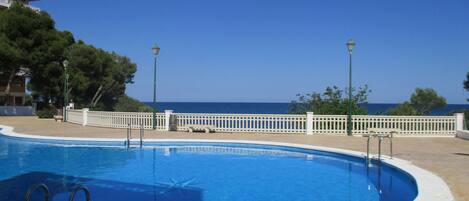 Una piscina con vista al mar, rodeada por una cerca blanca y árboles.