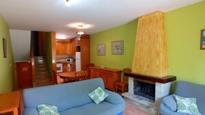 Een woonkamer met een open haard, een eethoek met houten kasten, en een keuken op de achtergrond.