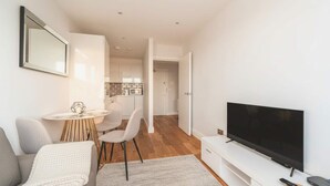 Een moderne woonkamer met een flatscreen televisie, een bank, een eettafel met stoelen en een keuken op de achtergrond.