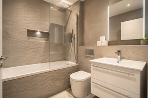 Un baño moderno con ducha de vidrio, inodoro blanco y tocador con espejo.