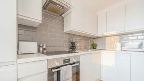 Een moderne keuken met witte kasten, een ingebouwde oven, een roestvrijstalen afzuigkap en een kleine potplant op het aanrecht.