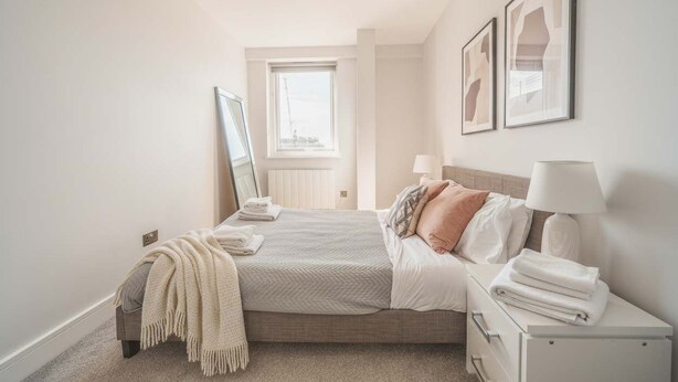 Een netjes ingerichte slaapkamer met een bed, nachtkastjes, een spiegel en lijstwerken aan de muur.