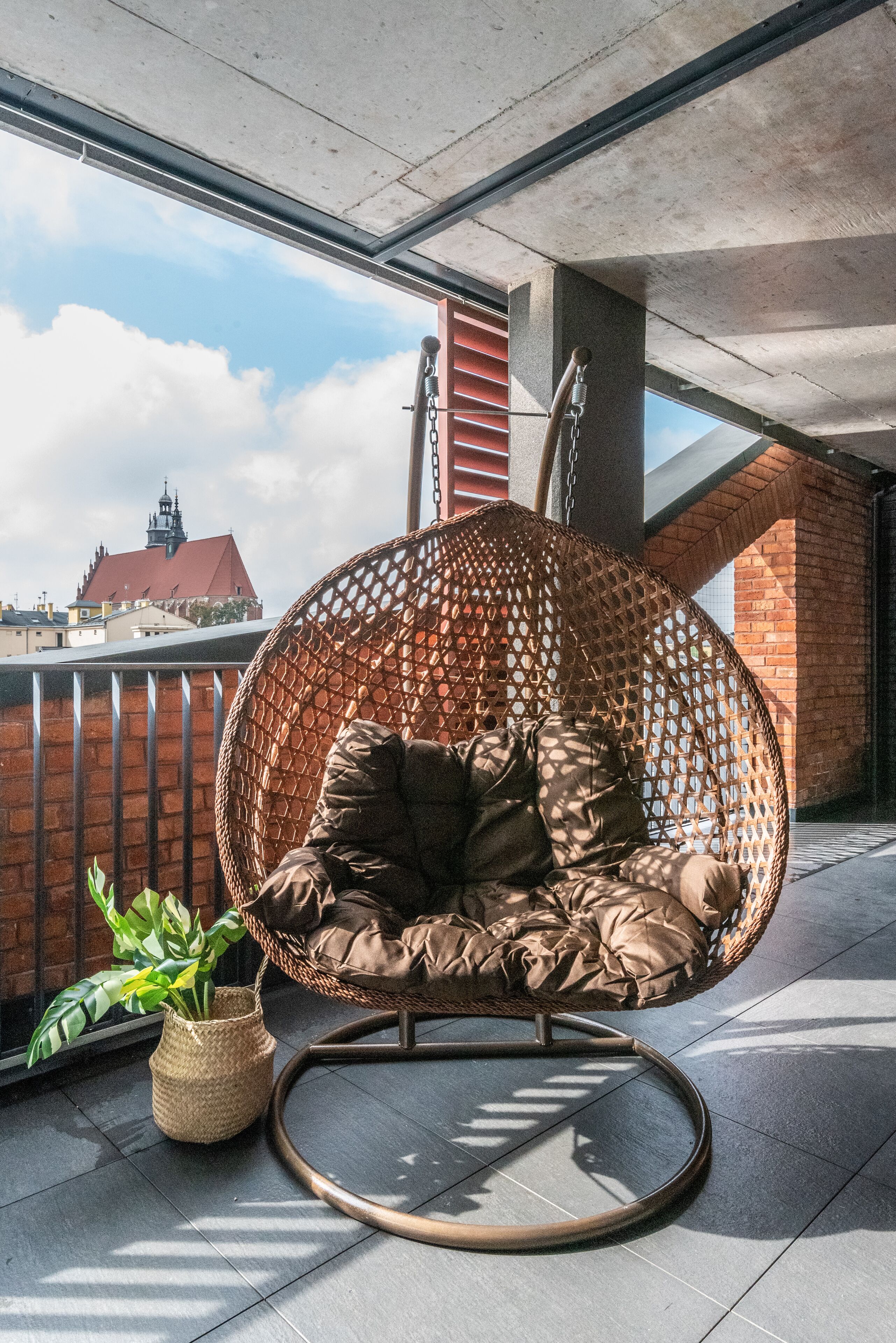A wicker chair with cushions on a balcony with a view of a building.
