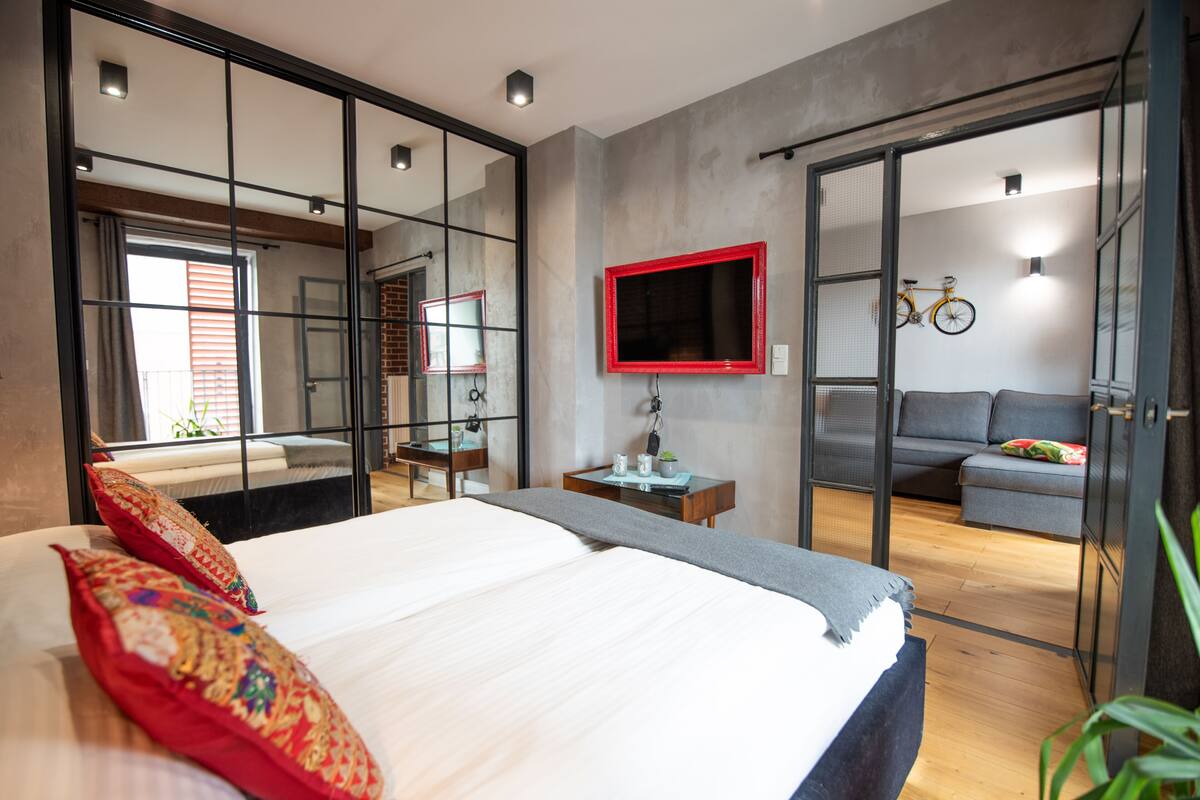Une chambre moderne avec un grand lit, un bureau, une télévision et un canapé dans la pièce adjacente.