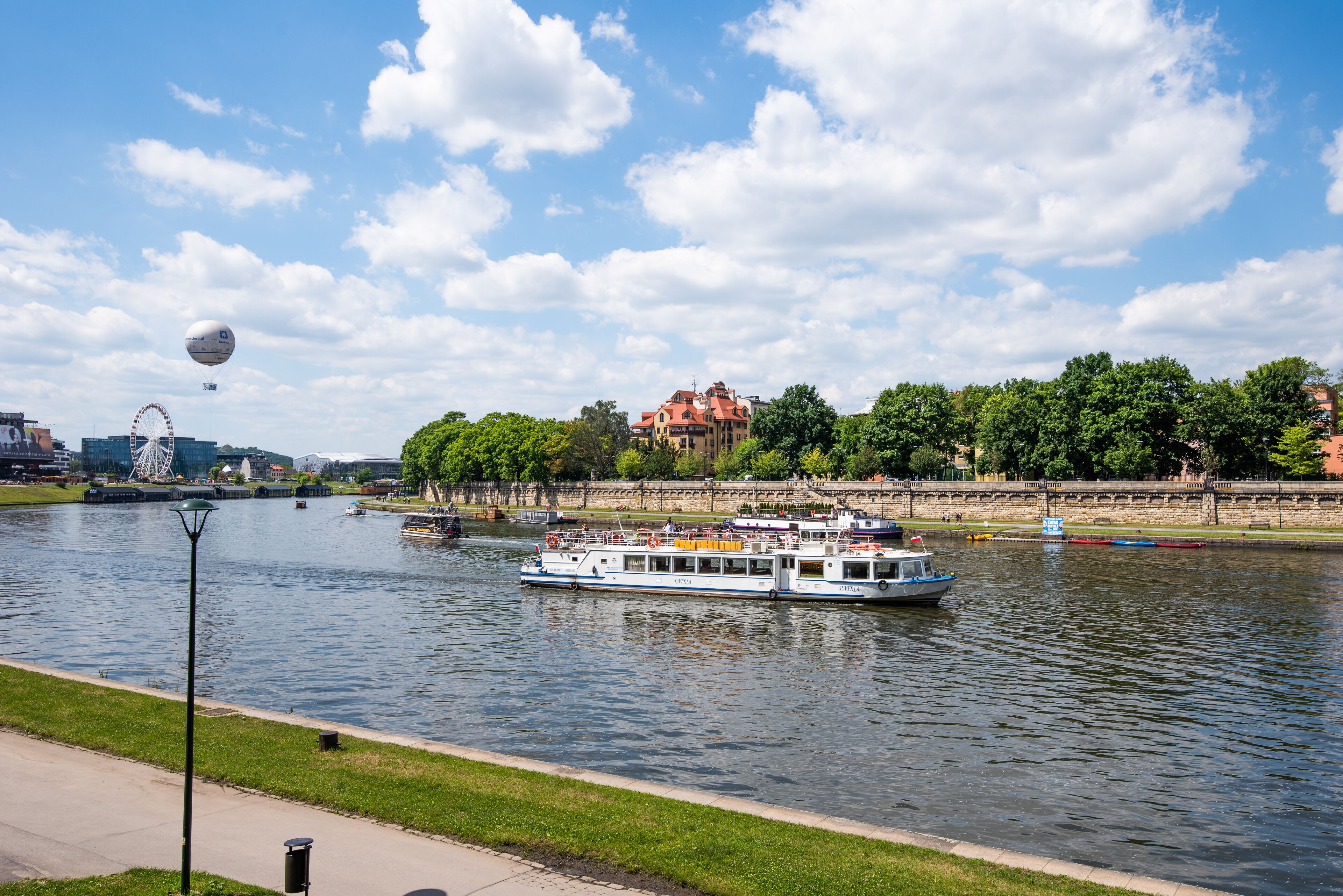 A river with a boat, a Ferris wheel, and buildings in the background.