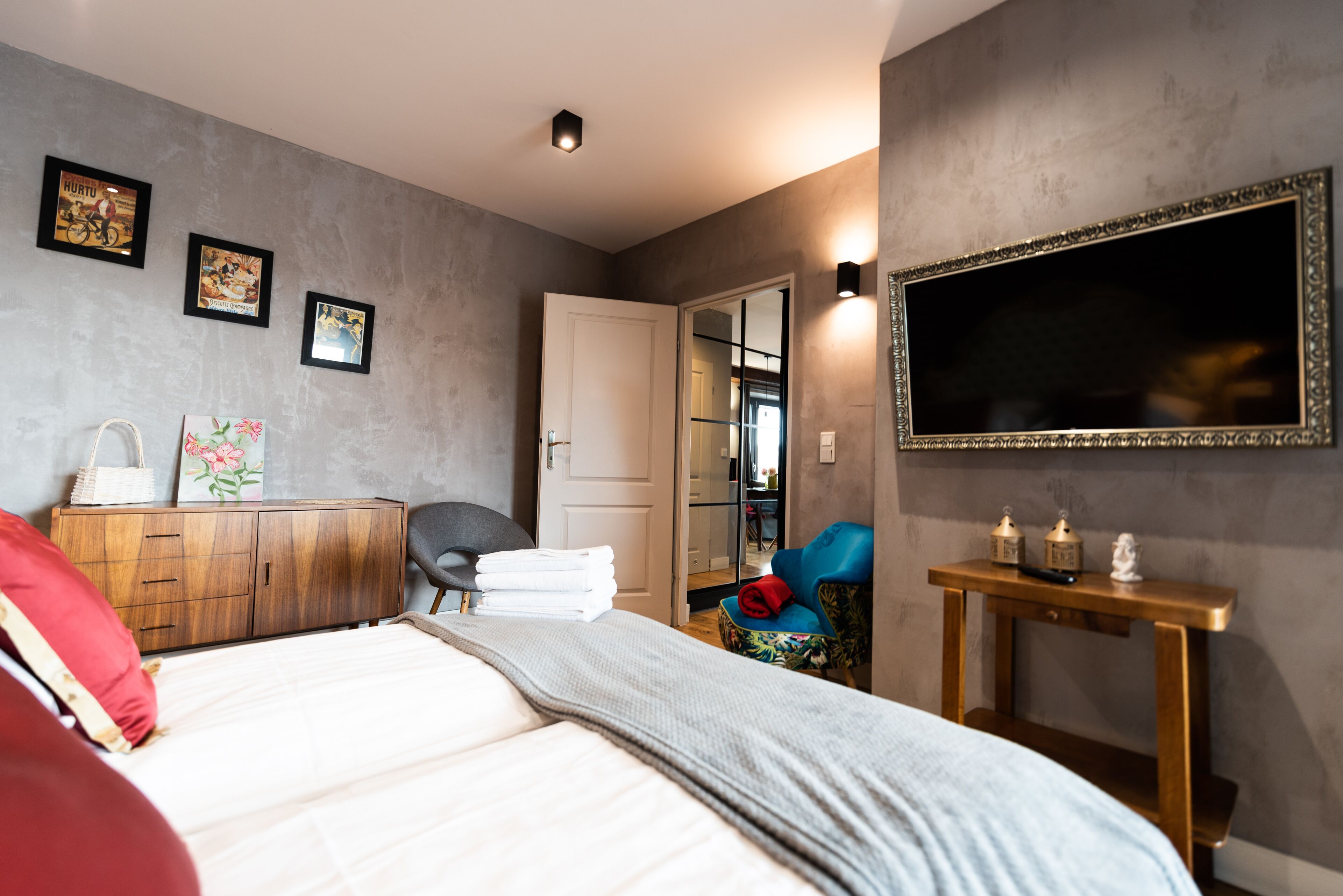 A bedroom with a bed, a wardrobe, a chair, a bedside table, and a mirror.