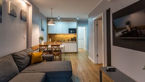 A modern living room with a grey sofa, a dining table, and a kitchen in the background. - City Lights Kazimierz (Kraków)