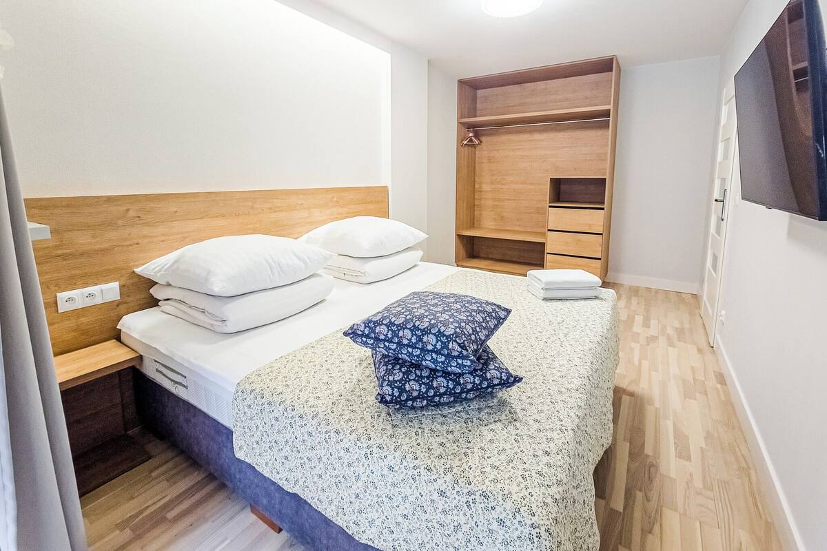 Une chambre à coucher avec un lit, une tête de lit en bois, une armoire intégrée et un téléviseur à écran plat fixé au mur.