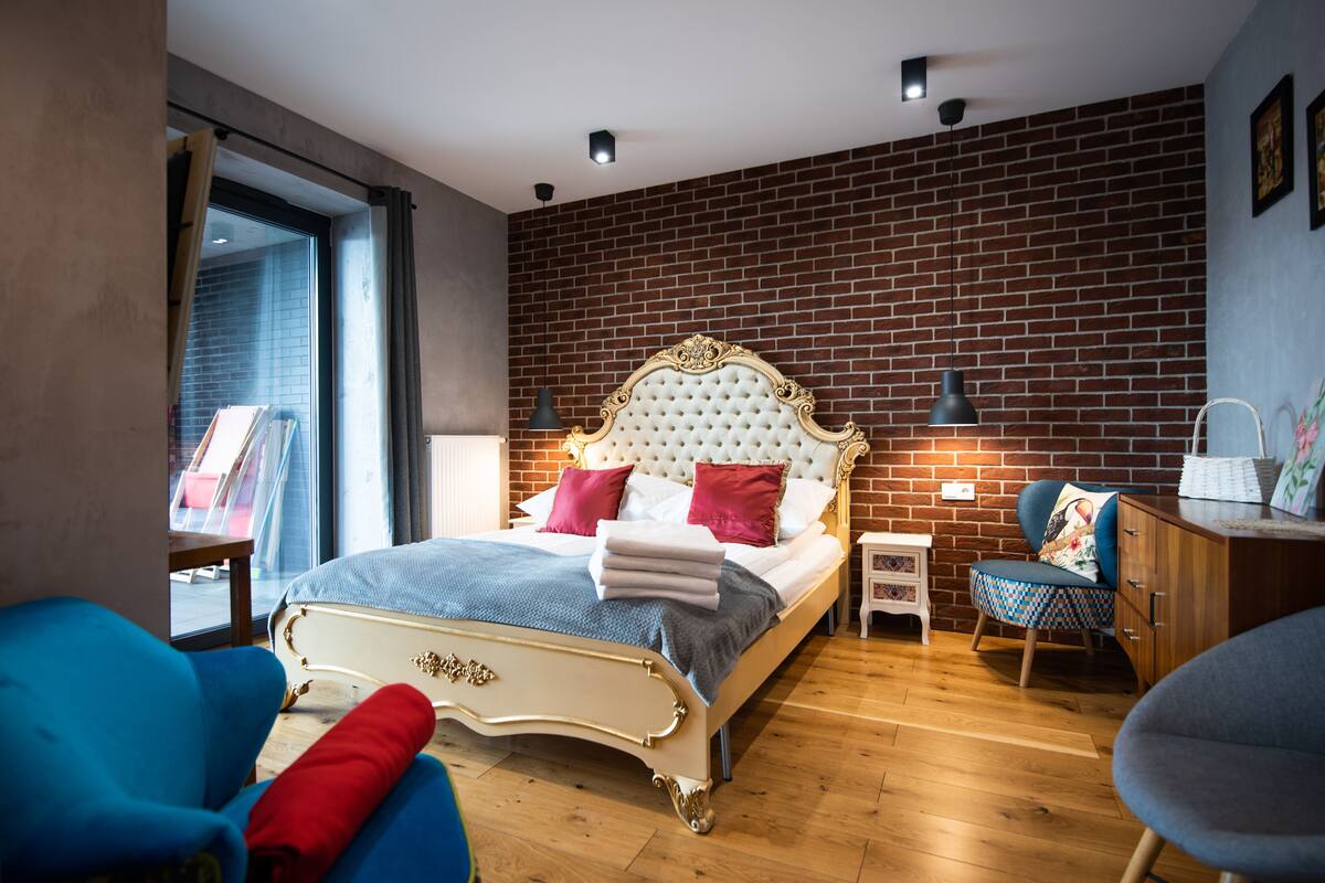 Une chambre avec un grand lit, une chaise bleue, une table de chevet en bois et un mur en briques.