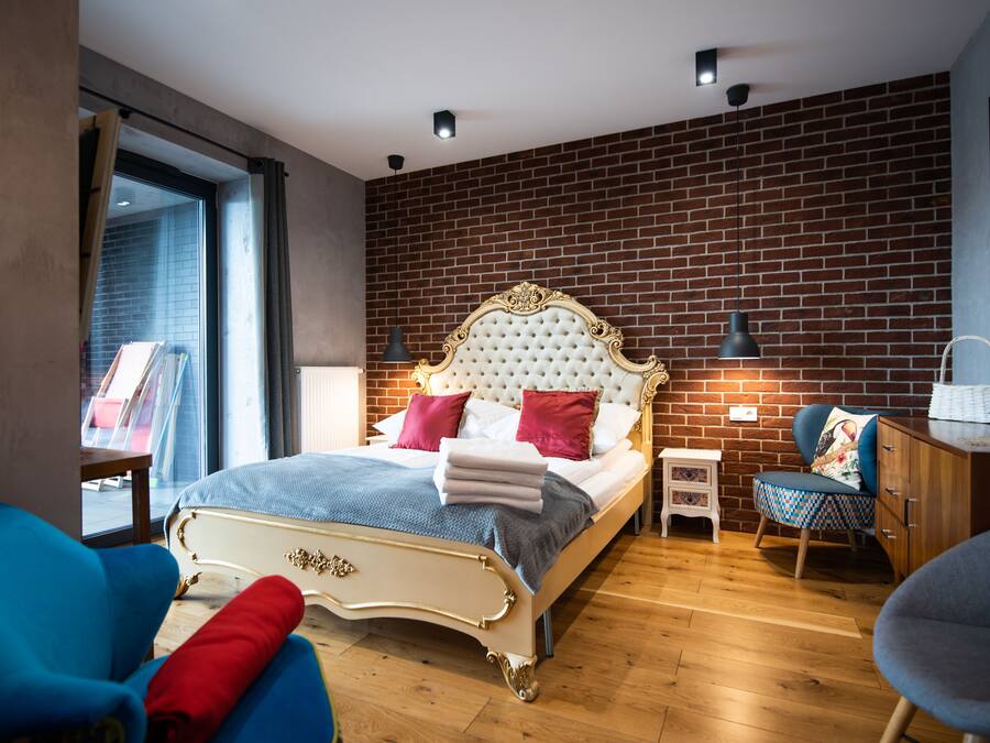 Une chambre avec un grand lit, une chaise bleue, une table de chevet en bois et un mur en briques.