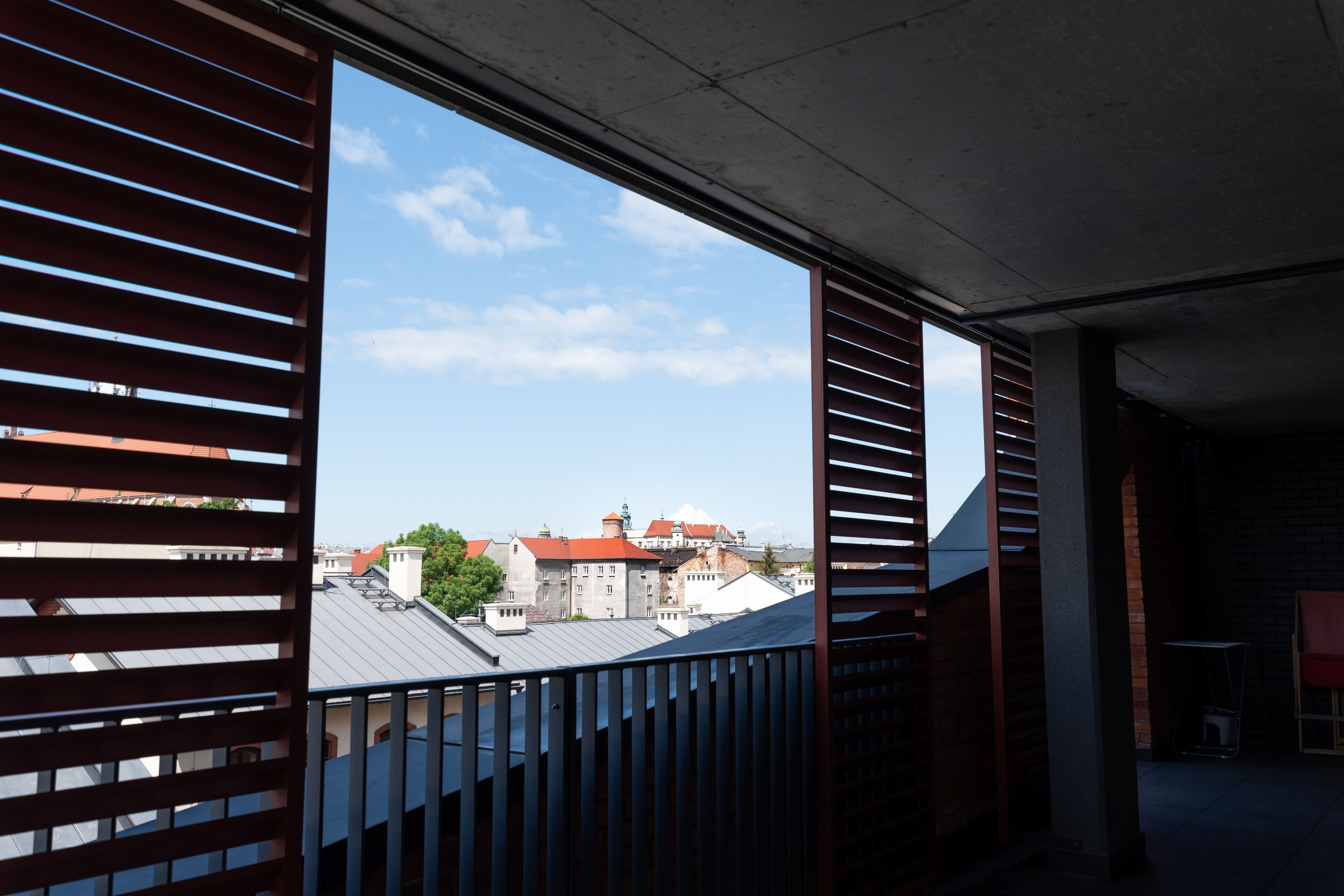 Uitzicht vanaf een balkon met metalen hekwerk, over een stadsbeeld met gebouwen en een heldere lucht.