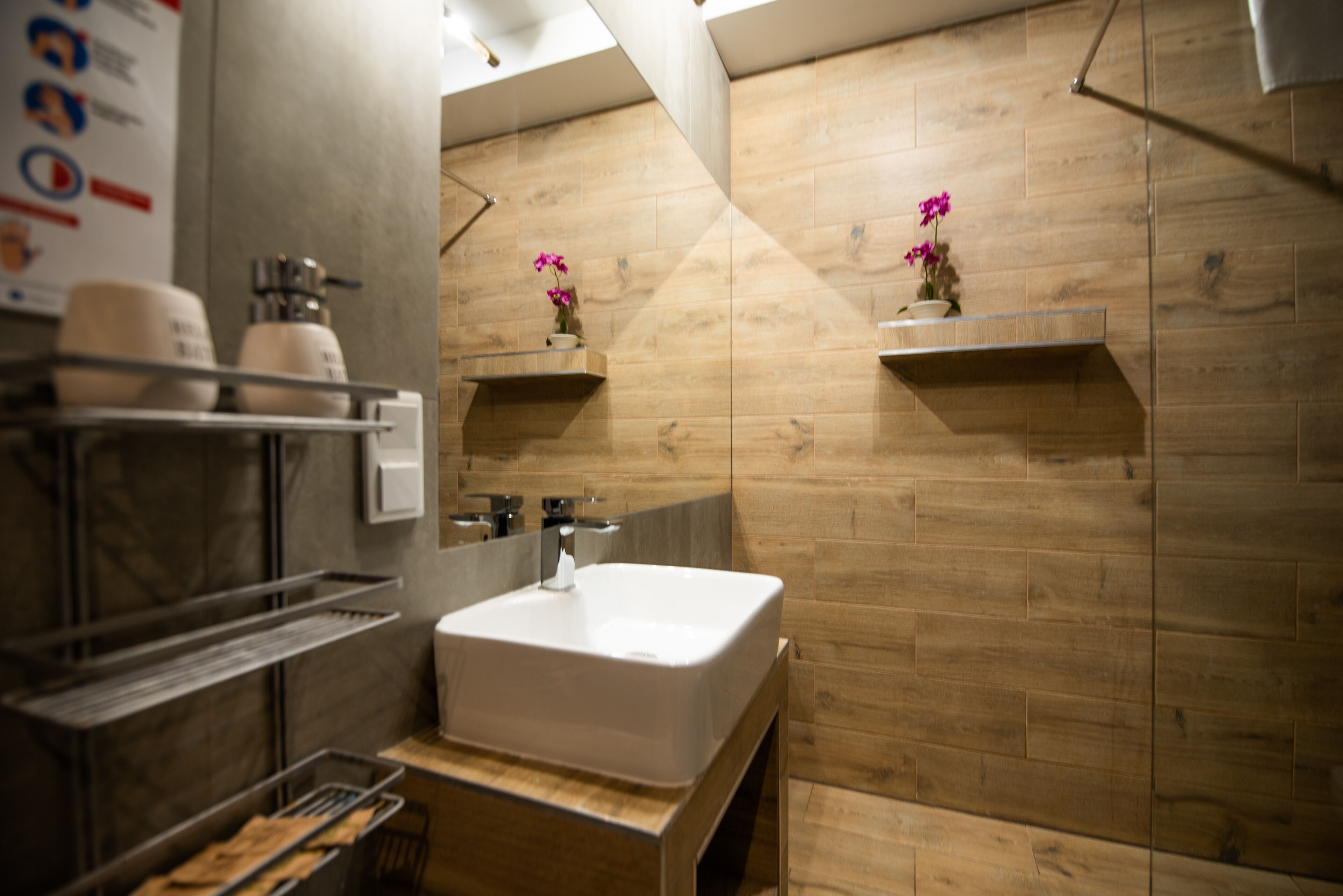 Ein modernes Badezimmer mit einem großen, weißen Waschbecken, Holzvertäfelung an den Wänden und zwei kleinen Regalen mit rosa Blumen.