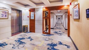 A hotel hallway with a patterned carpet, wooden paneling, and framed artwork on the walls. - Jinlong Hotel (Dongguan)
