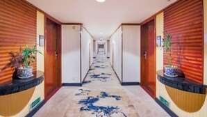 A hotel hallway with wooden paneling, potted plants, and a patterned carpet. - Jinlong Hotel (Dongguan)