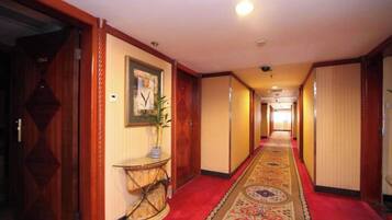 A hotel corridor with a red carpet, wooden doors, a framed picture, and a plant on a console table.