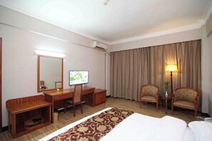 A hotel room with a bed, a desk with a computer, two chairs, a lamp, and a large window with curtains. - Jinlong Hotel (Dongguan)