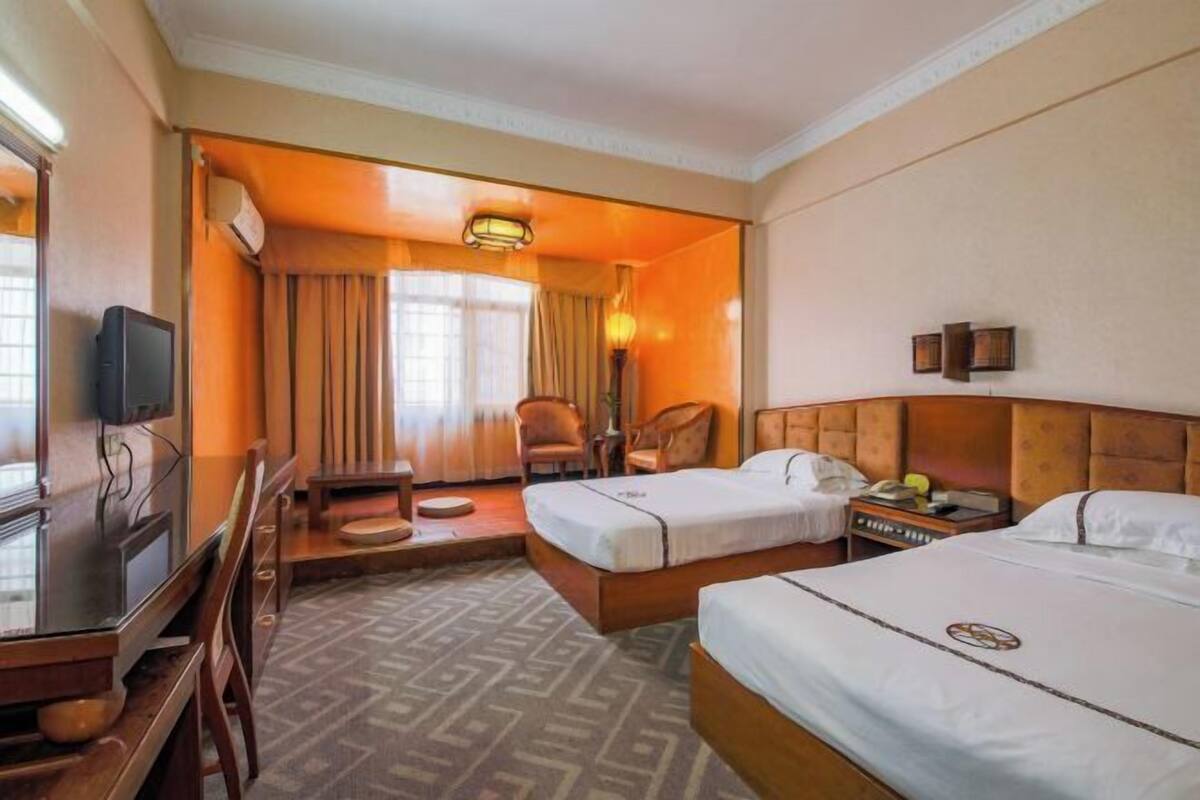 A hotel room with two beds, a desk, a chair, a television, and a window with curtains.