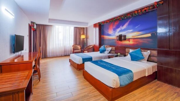 A hotel room with two beds, a desk, a TV, and a large painting on the wall. - Jinlong Hotel (Dongguan)