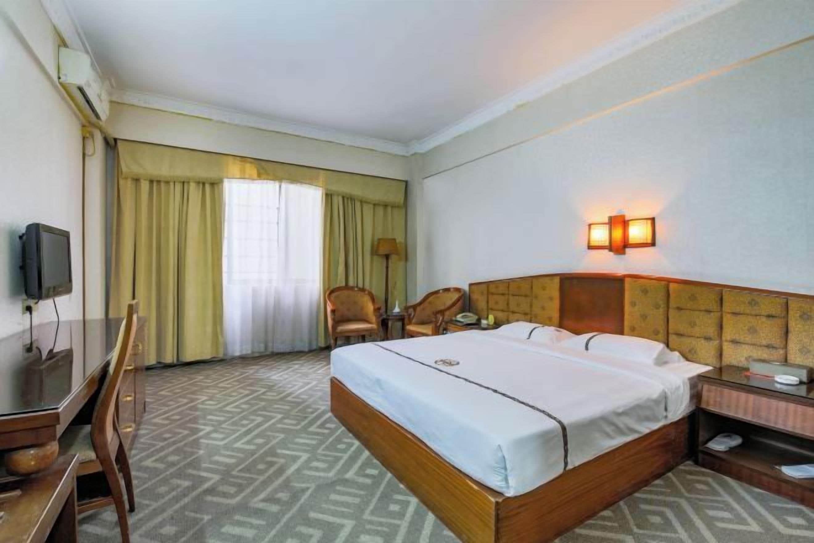 Een hotelkamer met een bed, bureau, stoel, televisie en een raam met gordijnen.