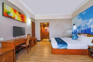 A hotel room with a bed, a desk, a chair, a television, and a painting on the wall. - Jinlong Hotel (Dongguan)