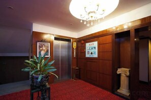 Et hotel lobby med rødt tæppe, en potteplante, elevator og en trævæg med en søjle.