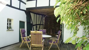 An outdoor patio with wooden chairs and a table, surrounded by white walls with black trim, and a wooden ceiling structure. - The small Villa OLEFant in the historic center of Schleiden Olef (Schleiden)