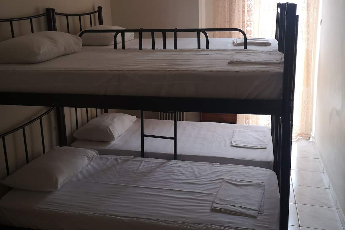 A dormitory room with bunk beds, a window with curtains, and a radiator.