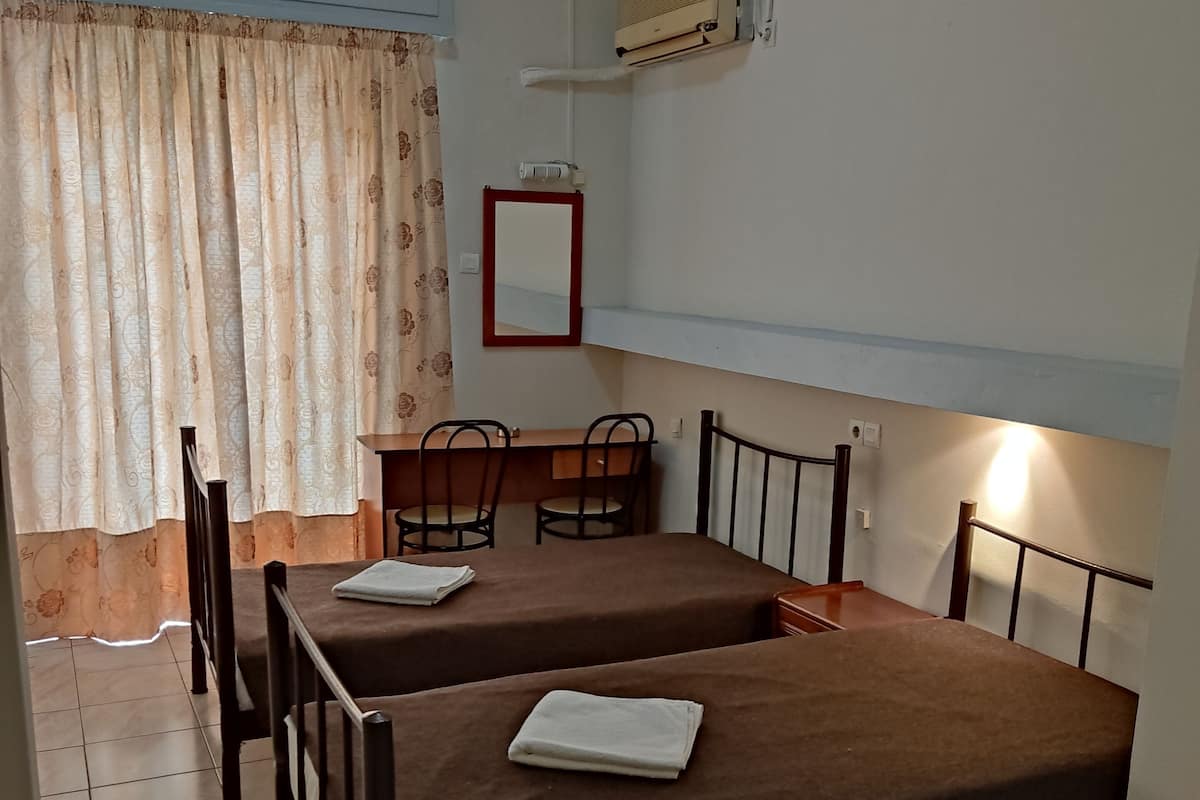 A room with two single beds, a small table with chairs, a mirror, and an air conditioning unit.