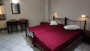 A room with a bed, two bedside tables, a desk with chairs, a mirror, and an air conditioning unit.