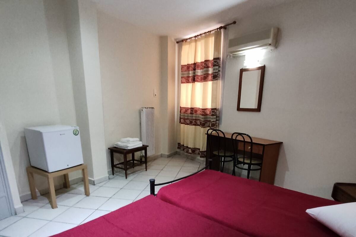 A bedroom with a bed, a desk, a chair, a radiator, and a white appliance.