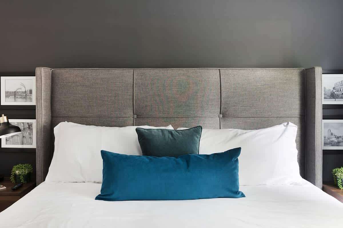 A bed with white and teal pillows, a dark headboard, and framed pictures on the wall.