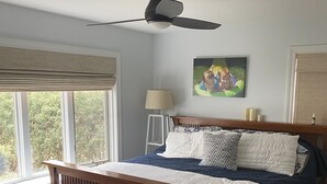 A bedroom with a wooden bed, a ceiling fan, a window with blinds, a bedside lamp, and a painting on the wall. - Beautiful lakefront view on Lauderdale Lakes only steps away from golf course.  (Elkhorn)