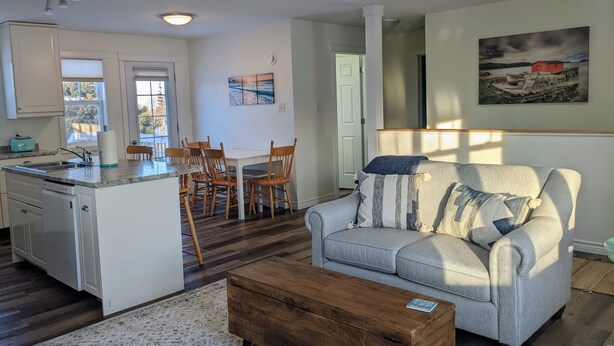 Een moderne keuken met een centraal eiland, houten eetstoelen, een grijze bank met gestreepte kussens en een houten salontafel.