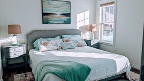 Een slaapkamer met een bed, twee nachtkastjes, een raam en een schilderij aan de muur.