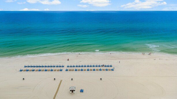 A beach with rows of blue chairs and a small structure, likely a lifeguard station, on the sand.