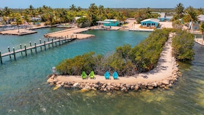Zona costera con un muelle, agua cristalina y una pequeña isla con sillas.