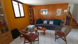 A cozy living room with a sofa, two wicker chairs, a coffee table, and a bookshelf.