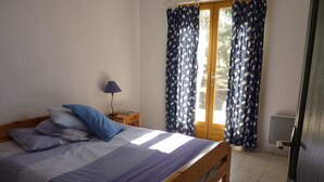 A bedroom with a bed, pillows, a nightstand, a lamp, and curtains.