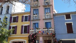 A multi-story building with balconies, a shop on the ground floor, and a clear blue sky.
