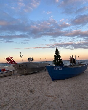 Dos barcos en una playa arenosa, cielo despejado y un árbol de Navidad.