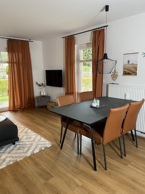 A modern dining area with a black table, brown leather chairs, a black pendant light, and a view of greenery outside. - Bella Casa Baabe (Ostseebad Baabe)