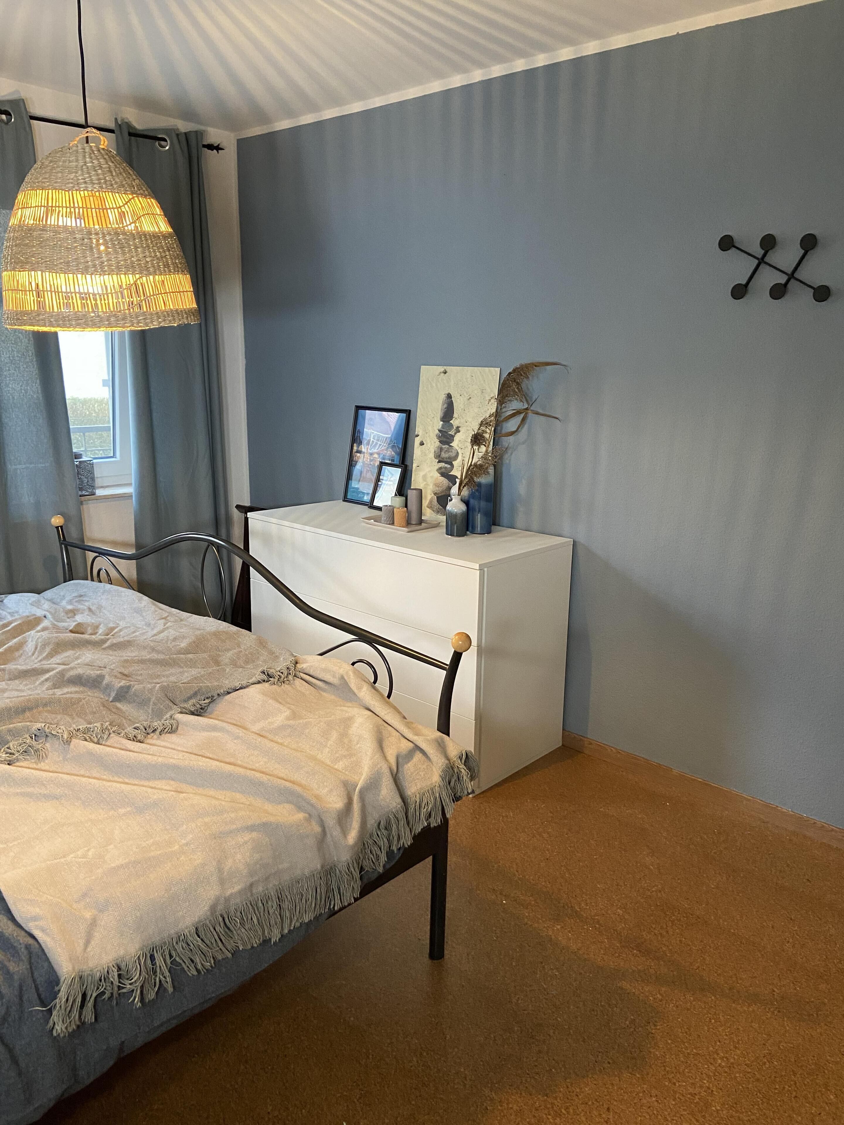 Une chambre à coucher comprenant un lit, une table de chevet, une lampe suspendue et un élément décoratif fixé au mur.