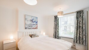 Ein Schlafzimmer mit Bett, Nachttischen, einem Gemälde, einem Fenster mit Vorhängen und einer Pendelleuchte.